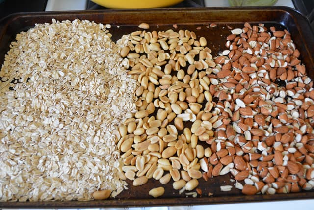 Energy bar ingredients, oats, peanuts, and almonds on a baking sheet.