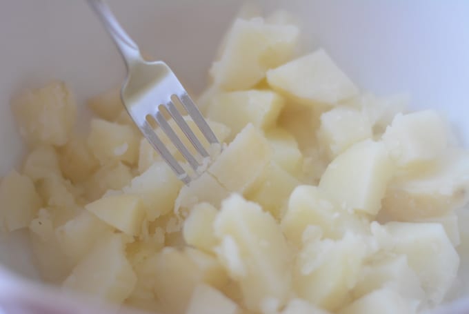 Mashing cooked potatoes with a fork.