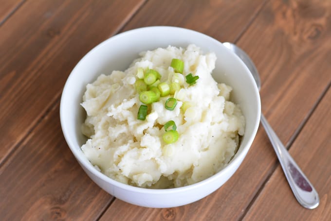 Made from scratch mashed potatoes topped with diced scallions in a white bowl.