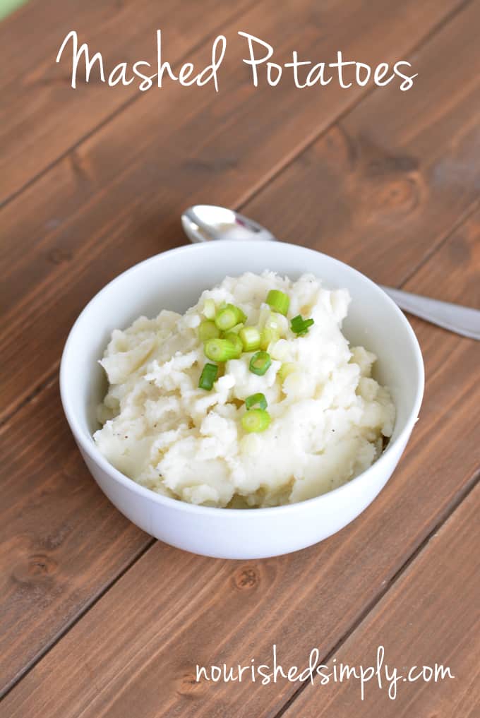 Mashed Potatoes homemade in a white bowl with a spoon with chopped scallion on top.