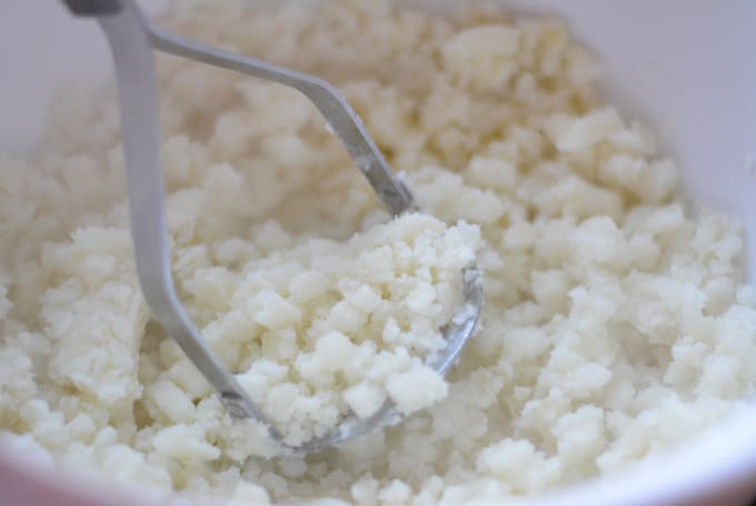 A potato masher mashing cooked potatoes.