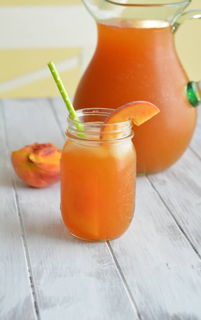 A pitcher of iced tea behind a mason jar filled with peach iced tea.