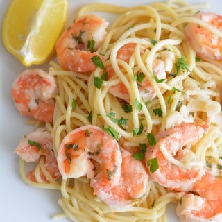 Shrimp scampi on a white plate with two lemon wedges.