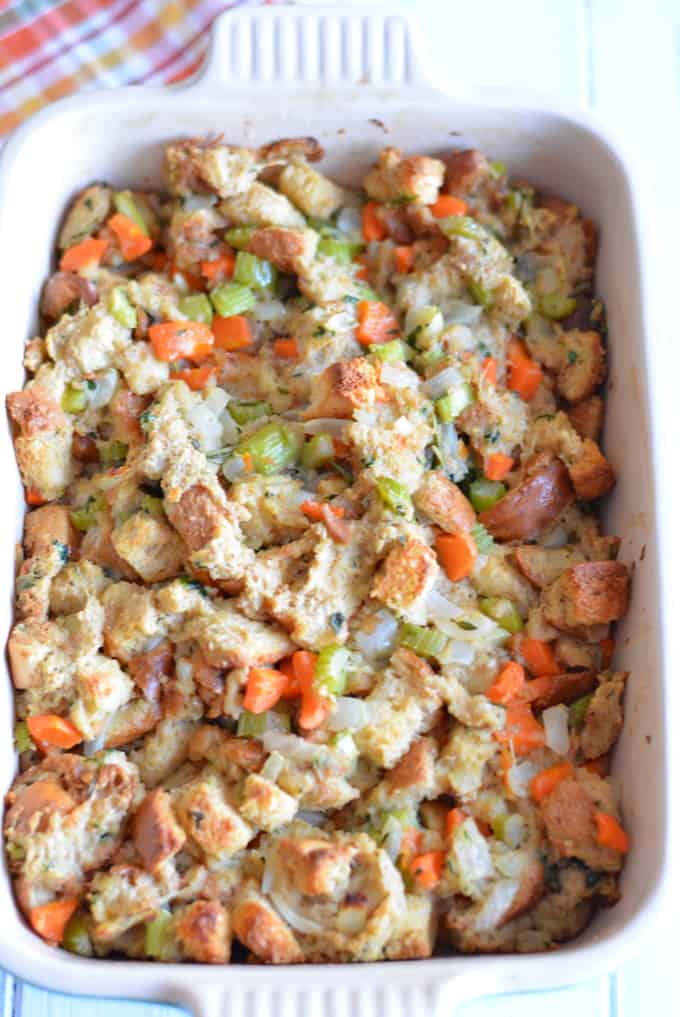 Stuffing made with whole wheat bread, carrot, onion, and celery baked in a white baking pan.