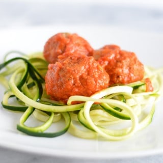 Meatless balls made with eggplant on top of zucchini noodles on a white plate.