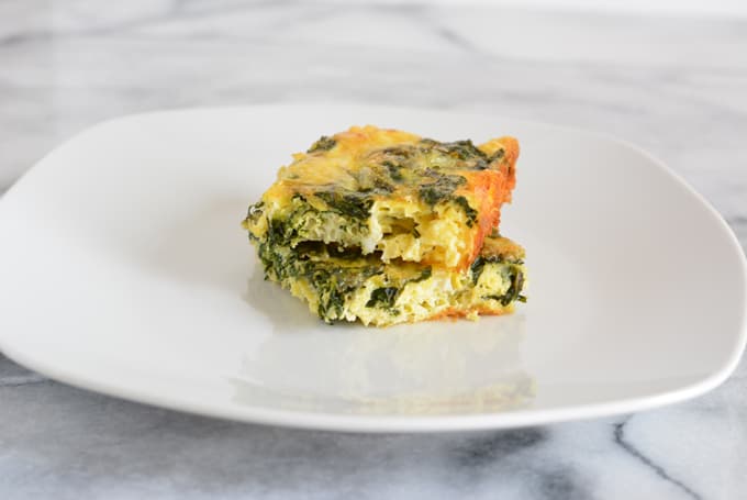 Two squares of a crustless fittata with kale on a white plate.