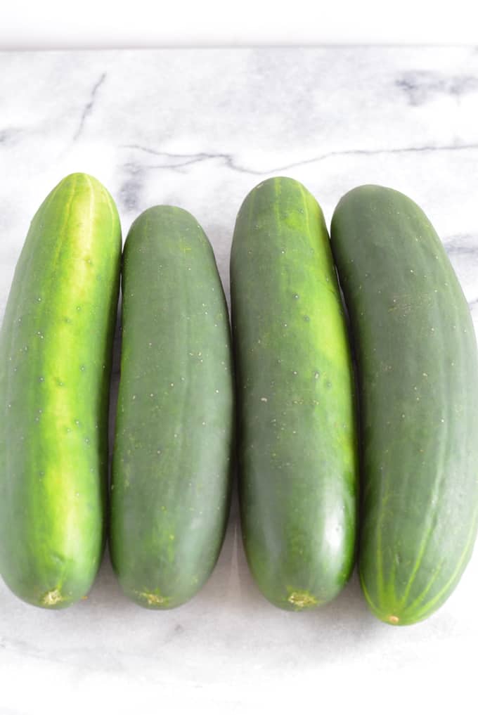 Four cucumbers on a white marble counter.