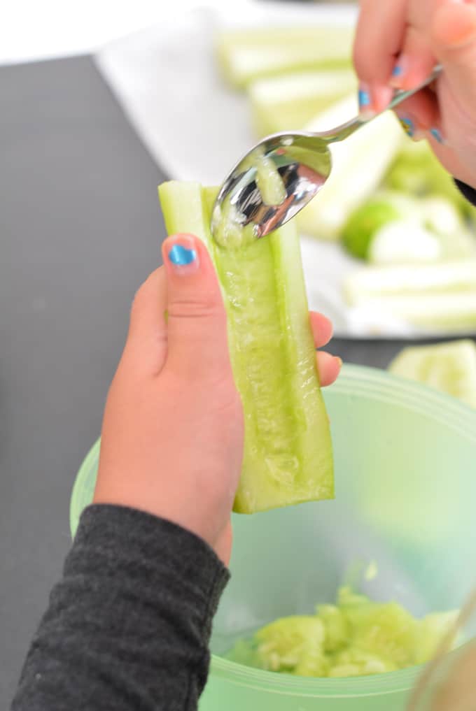 A girl scooping seeds out of a cucumber with a spoon.