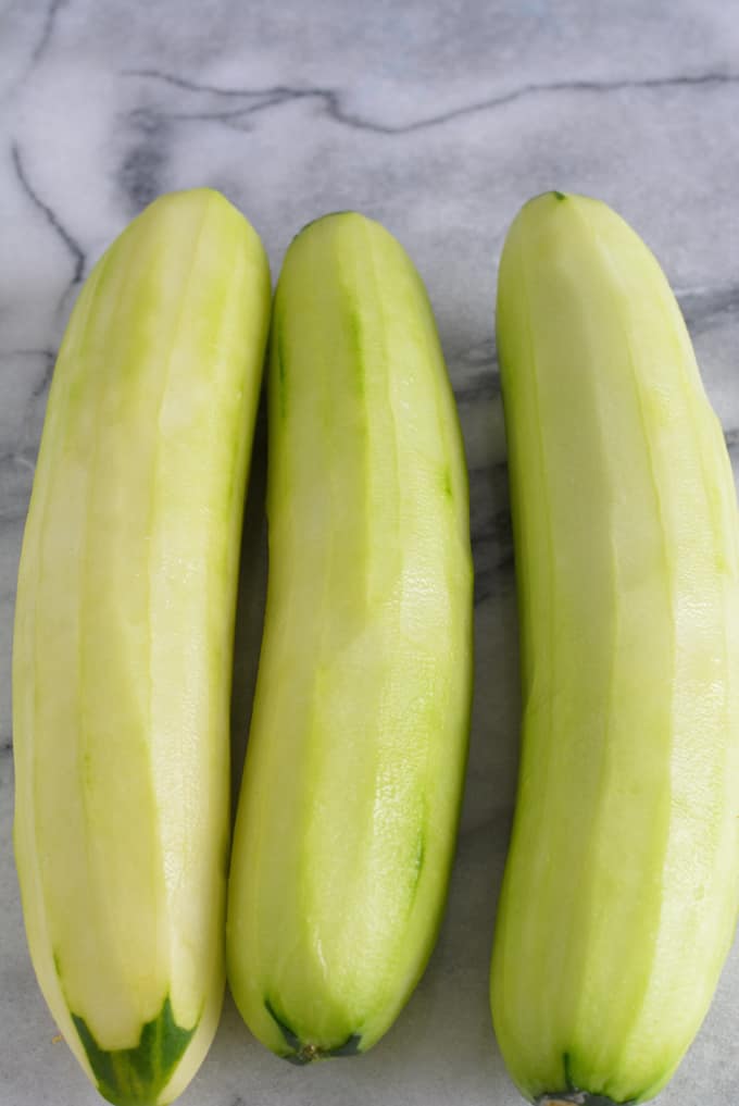 Three cucumbers peeled sitting on a white marble table.