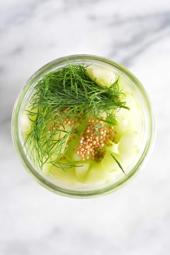 Cucumber slices in a mason jar with fresh dill and mustard seed on top.