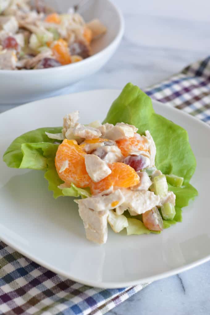 A scoop of chicken salad on top of butter lettuce on a white plate.