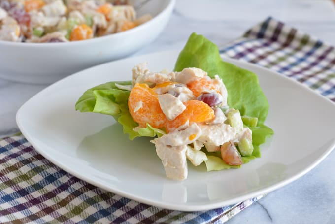 Chicken salad mixed with grapes and mandarin oranges on a white plate next to a white bowl with additional chicken salad.