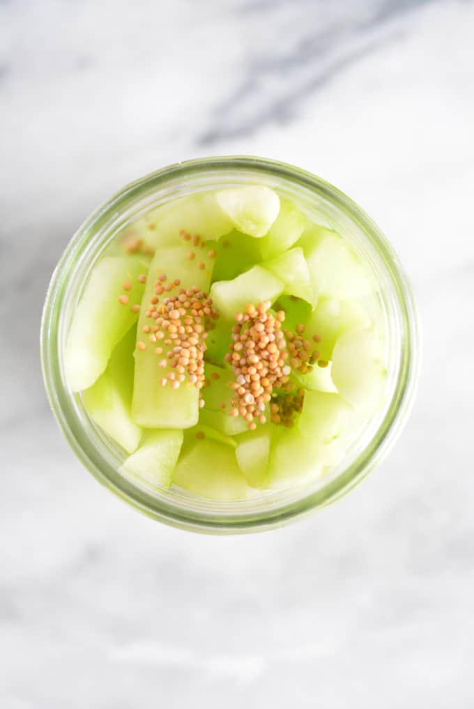 Cucumber slices inside mason jar with mustard seed on top.