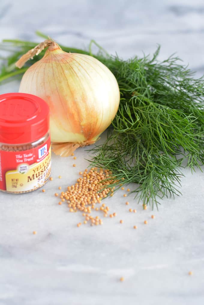 Fresh dill, onion, and mustard seed on a white counter.