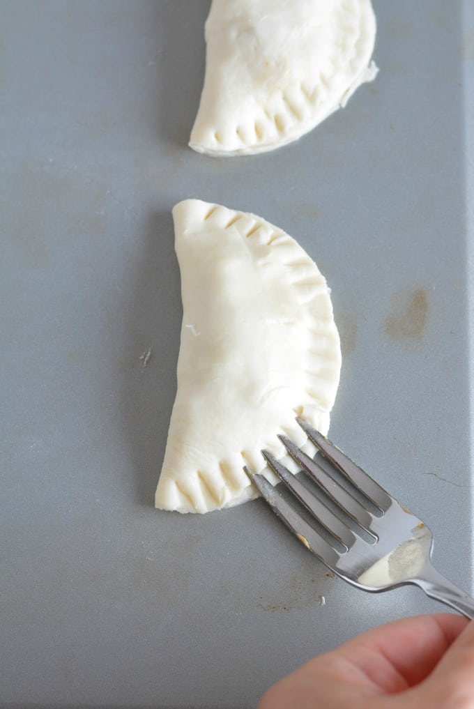 An uncooked Empanada being pressed closed with the back of a fork.