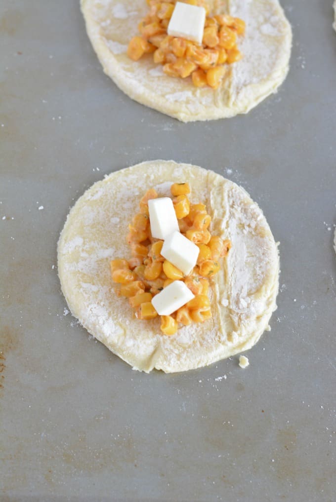 Corn and cheese on top of circles of dough placed on a baking sheet.