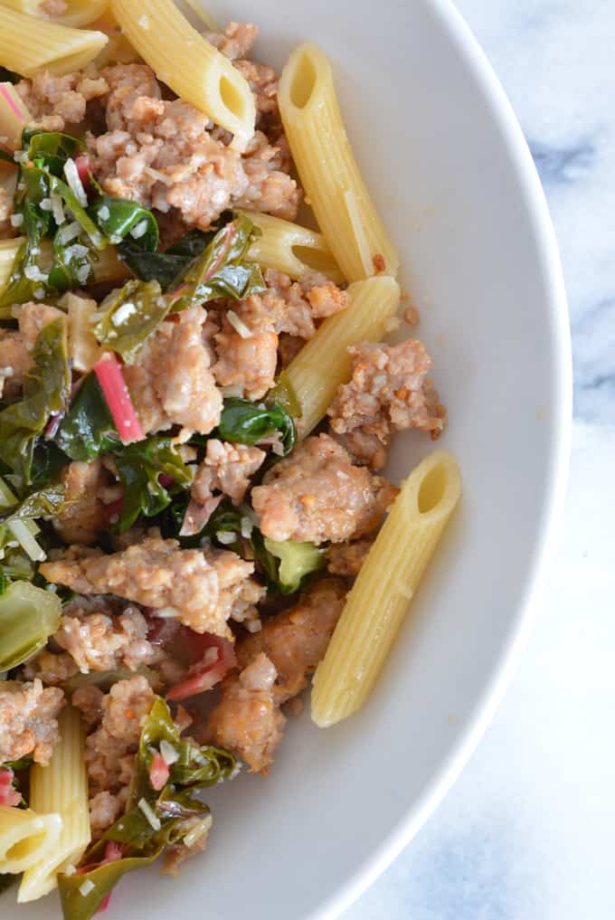 Sausage with Garlic Swiss Chard with penne pasta in a white bowl.