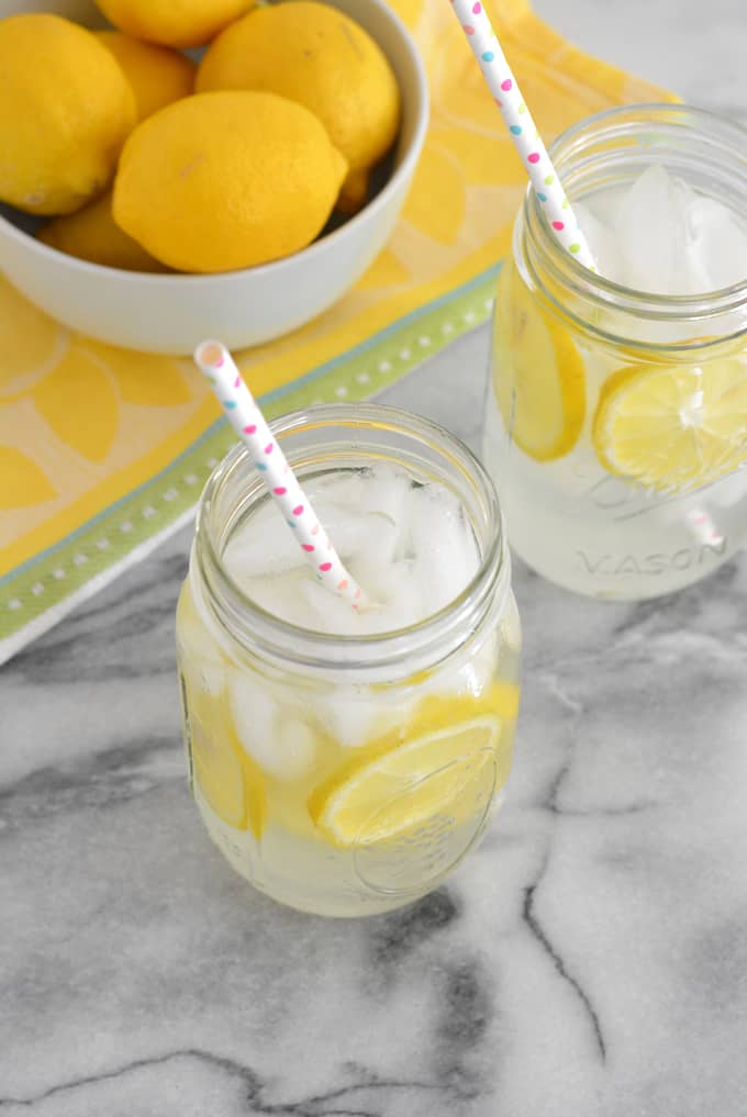 Two mason jars filled with fresh lemonade next to a bowl of lemons.