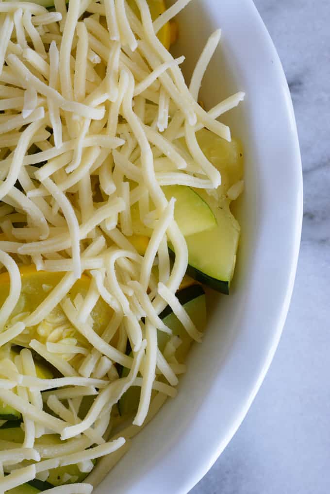 Sliced zucchini and yellow squash in a white dish topped with shredded white cheese.