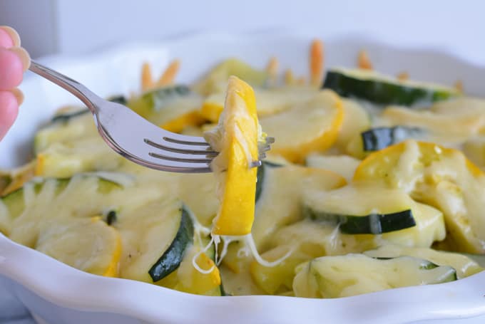 A fork full of baked squash with gooey gruyere cheese in a white dish.