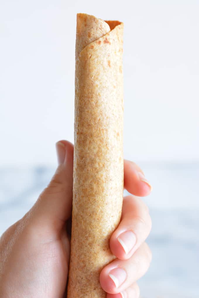 A breakfast taquito held in a woman's hand.