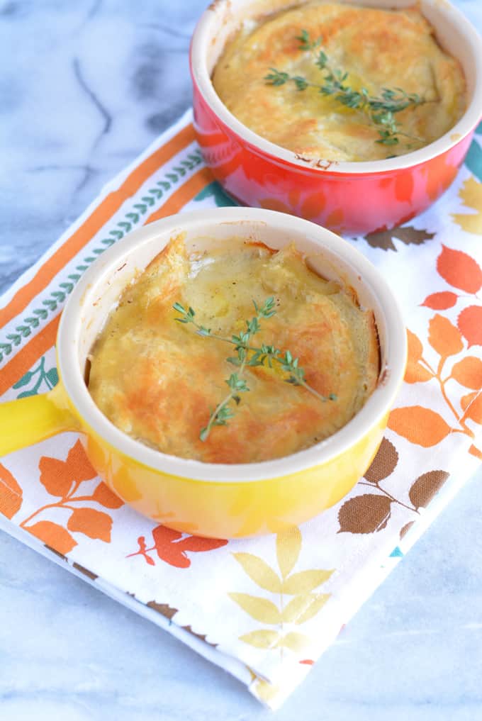 One yellow and one red bowl filled with turkey pot pie topped with crust and thyme leaves.