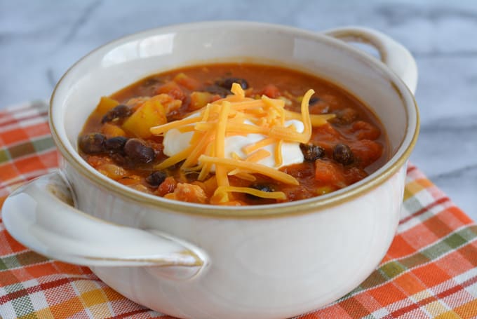 Leftover Turkey & Pumpkin Chili topped with cheddar cheese and sour cream in a white bowl.