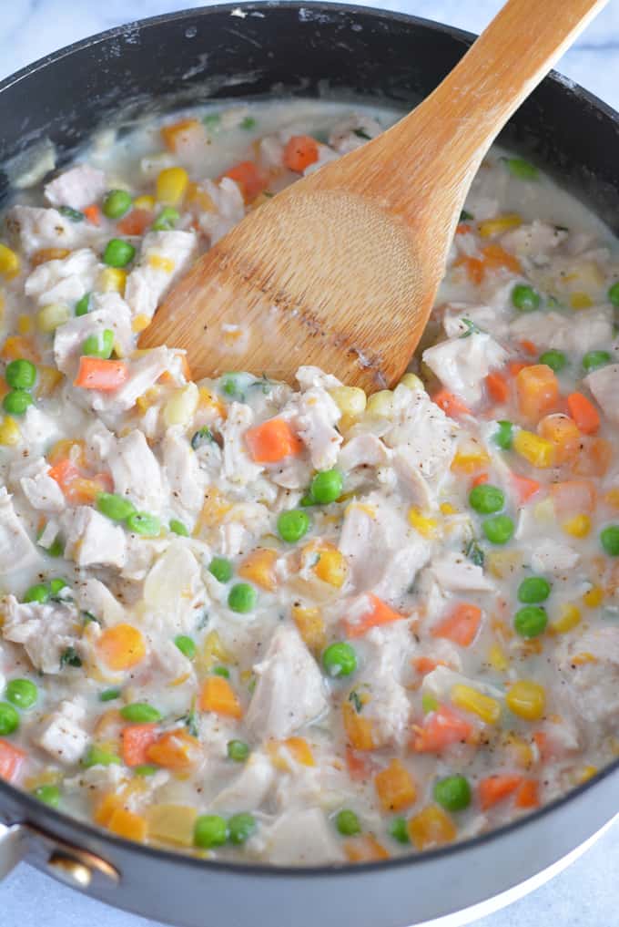 Turkey with carrots, peas, corn and squash in a creamy sauce in a saute pan with a wood spoon.