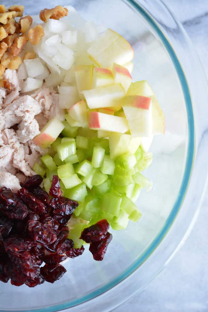 A glass bowl with chopped apple, celery, onion, walnuts, turkey and dried cranberries.