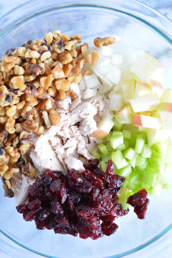 Diced turkey, walnuts, dried cranberries, celery, onion, and chopped apples in a glass bowl.