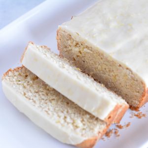 A sliced glazed lemon loaf on a white plate.