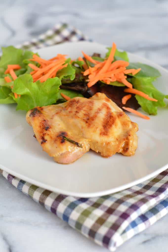 Grilled Maple Dijon chicken Thighs on a white place next to a green salad.