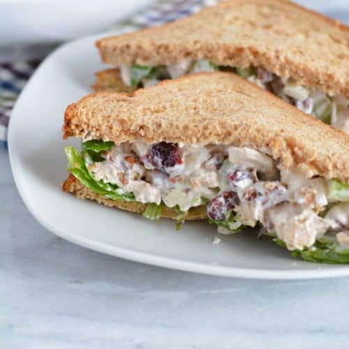 Chicken salad on whole wheat bread on a white plate.