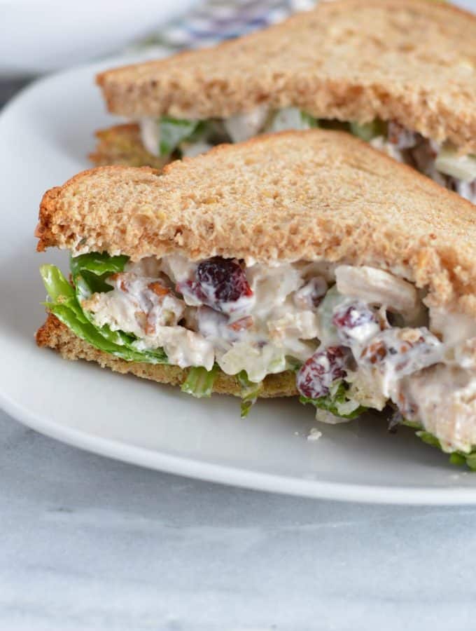 Chicken salad on whole wheat bread on a white plate.