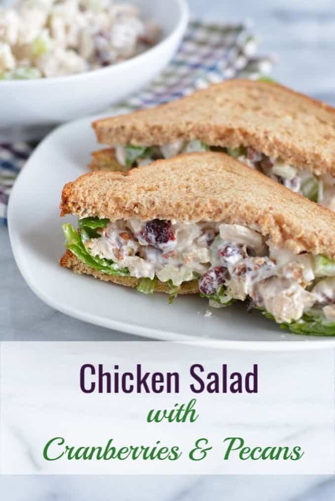 Pecan and cranberry chicken salad sandwich on wheat bread cut in half on a white plate.