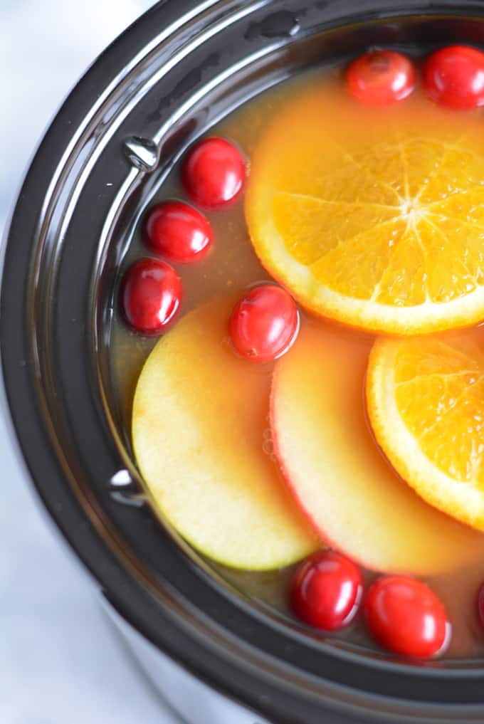 Hot apple cider with apple, oranges, and cranberries in a slow cooker