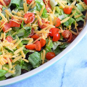 Taco dip topped with cheese, lettuce and tomatoes.